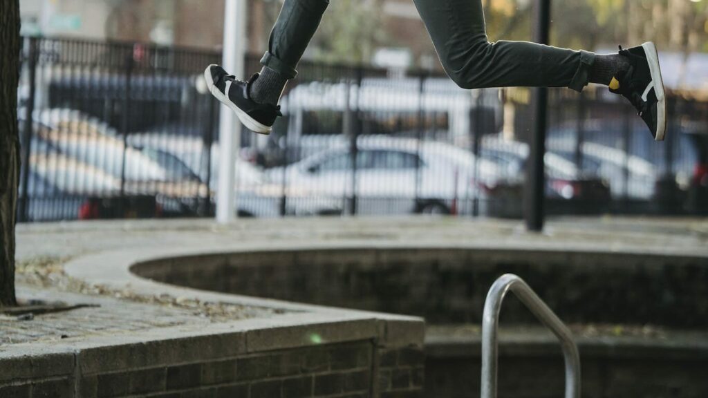 Full body back view of sportive male jumping above ground in street during parkour exercise against blurred buildings in city